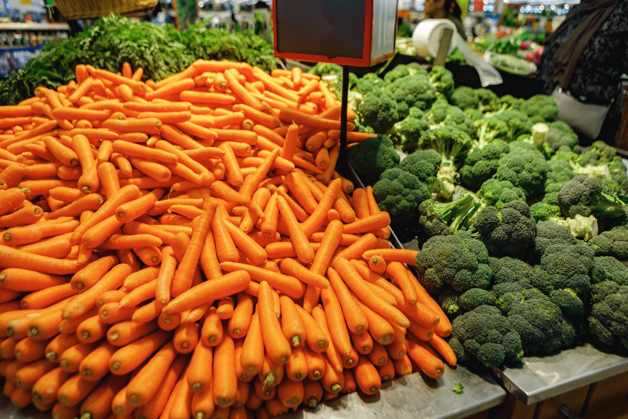 Pile of fresh carrots and broccoli on counter in supermarket